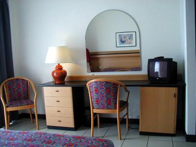 Ein Hotelzimmer mit zwei Stühlen, einem Schreibtisch, einem Spiegel und einem Fernseher.