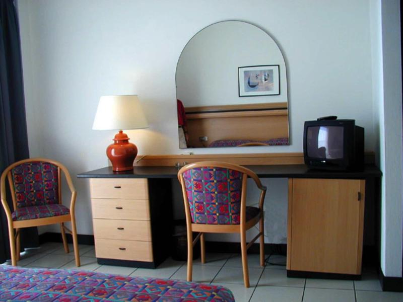 Ein Schreibtisch mit zwei bunten Stühlen, einer Lampe, einem alten Fernseher und einem Spiegel an der Wand.