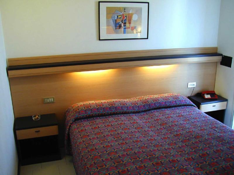 Ein einfaches Schlafzimmer mit großem Bett, Holzkopfteil, Nachttischen und einem Bild an der Wand.