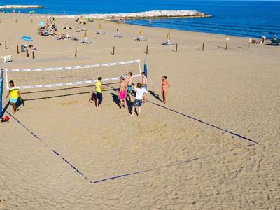 Menschen spielen Beachvolleyball am Sandstrand mit klarem blauem Meer im Hintergrund.
