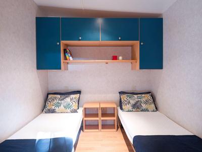 Kleines Hotelzimmer mit zwei Einzelbetten, Nachttisch und blauen Hängeschränken