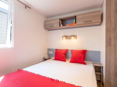 Kleines Schlafzimmer mit Doppelbett, roten Kissen, Holzmöbeln und Fenster rechts.