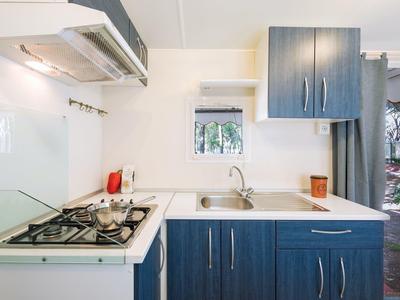 Kleine Küche mit blauem Unterschrank, Gasherd und Spüle neben Fenster.