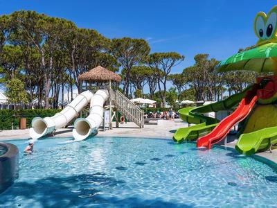 Kinderplanschbecken mit bunten Rutschen und Wasserspielen in einer Hotelanlage bei Sonnenschein.