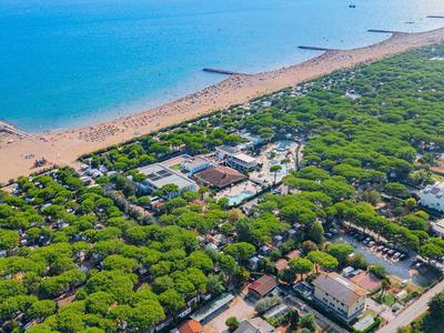 Luftaufnahme einer bewaldeten Küstenregion mit Strand und blauer Meereslinie am Horizont.