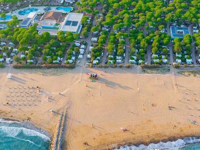 Breiter Sandstrand mit Liegestühlen, dahinter grüne Bäume und einige Gebäude am Meer.