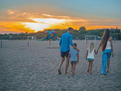 Familie mit zwei Kindern geht bei Sonnenuntergang barfuß am Strand entlang.