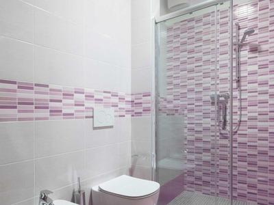 Modernes Badezimmer mit rosa Fliesen, Bidet, Toilette und Duschkabine mit Glaswand.
