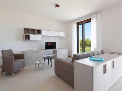 Helles Wohnzimmer mit gemütlichen Sesseln, TV und großen Fenstern mit Blick ins Grüne.