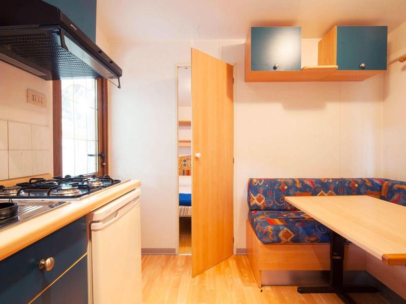 Kleine Küche mit Gasherd, offenem Holztürbereich und Sitzecke mit gemusterten Polstern.