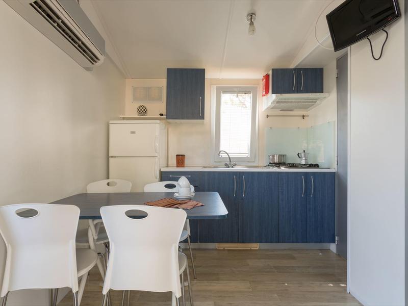 Kleine moderne Küche mit blauem Unterschrank und kleinem Esstisch mit weißen Stühlen.