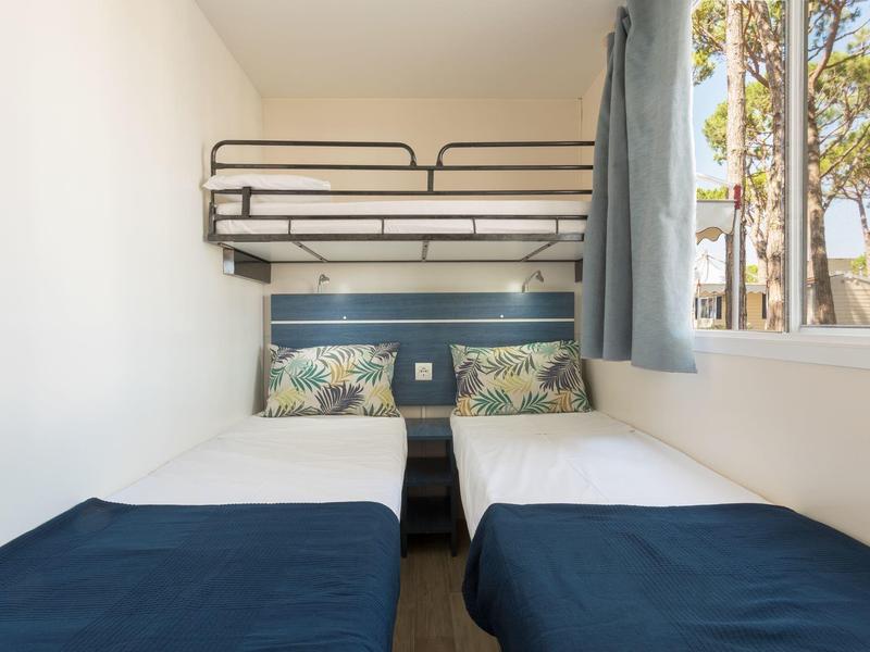 Kleines Schlafzimmer mit zwei Einzelbetten und einem Hochbett, Fenster mit Blick auf Bäume.