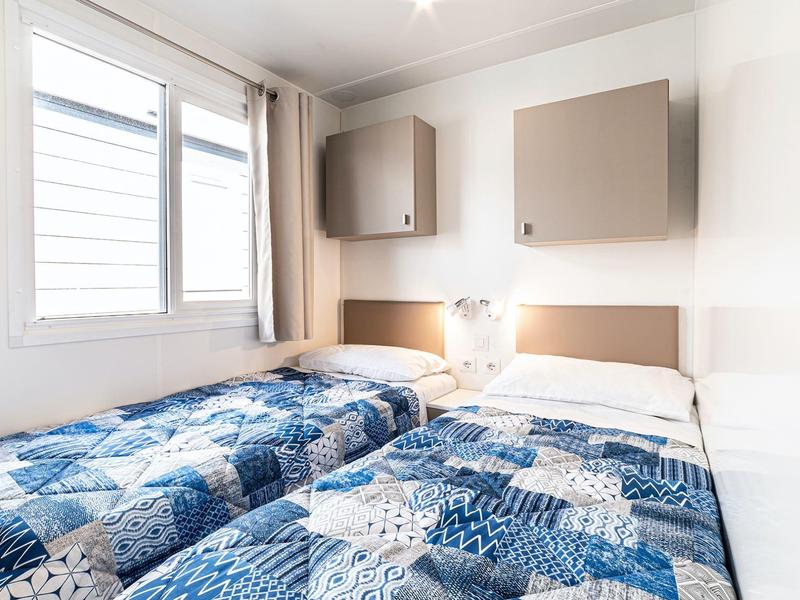 Kleines, helles Schlafzimmer mit zwei Einzelbetten und blauen Patchwork-Decken.