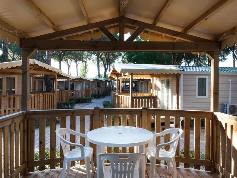 Überdachte Terrasse mit runder weißer Gartentisch und vier Stühlen, Blick auf Mobilheime und Bäume.