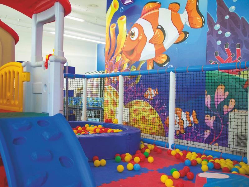 Bunter Indoor-Spielbereich mit Rutsche, Bällen und Wandgestaltung mit Meeresmotiven.