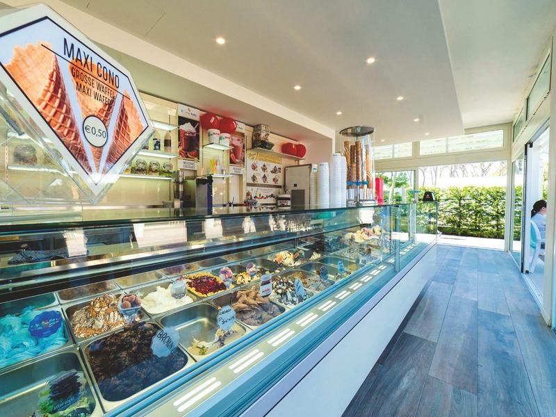 Modernes Eiscafé mit großer Glasvitrine voller bunter Eissorten und hellen Innenraum.