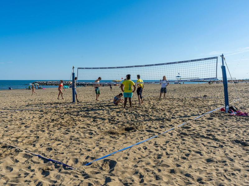 Mehrere Personen spielen Beachvolleyball auf sandigem Strand bei klarem Himmel.