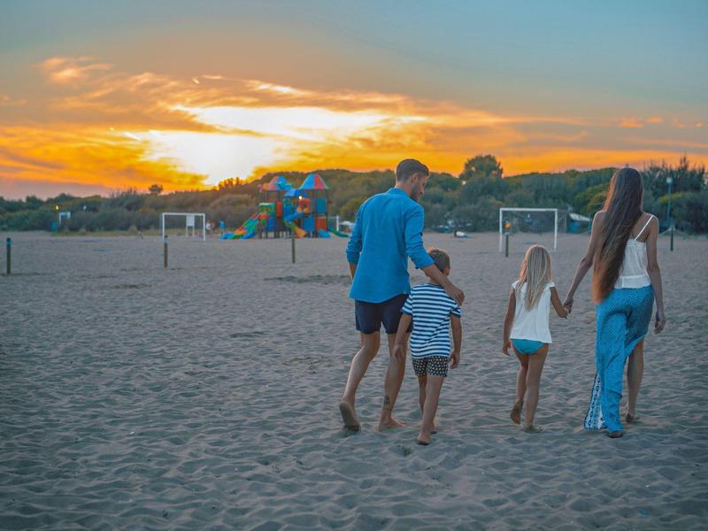Familie mit zwei Kindern geht bei Sonnenuntergang barfuß am Strand entlang.