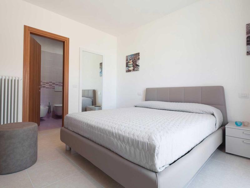 Modernes Schlafzimmer mit grauem Bett, weißer Bettdecke und offenem Badezimmer