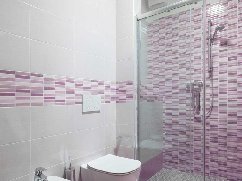 Modernes Badezimmer mit rosa Fliesen, Bidet, Toilette und Duschkabine mit Glaswand.