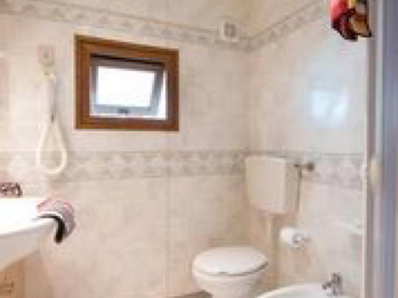 Kleines Badezimmer mit weißer Toilette, Bidet, Handtuchhalter, Fön und einem kleinen Fenster.
