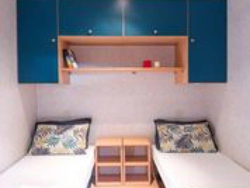 Kleiner Raum mit zwei Einzelbetten, blauen Wandschränken und kleinem Nachttisch in der Mitte.