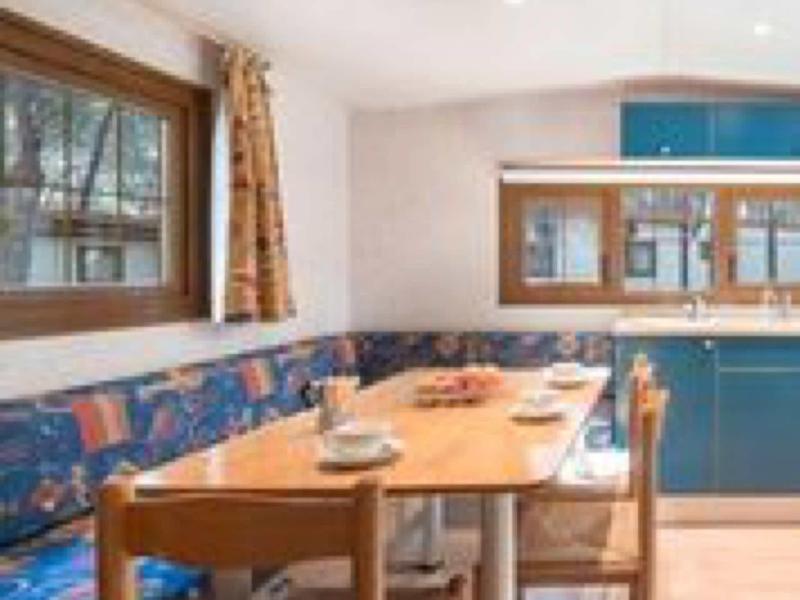 Gemütliche Eckbank mit blau gemustertem Stoff, Holztisch, Holzstühlen und Küchenzeile mit blauen Schränken.