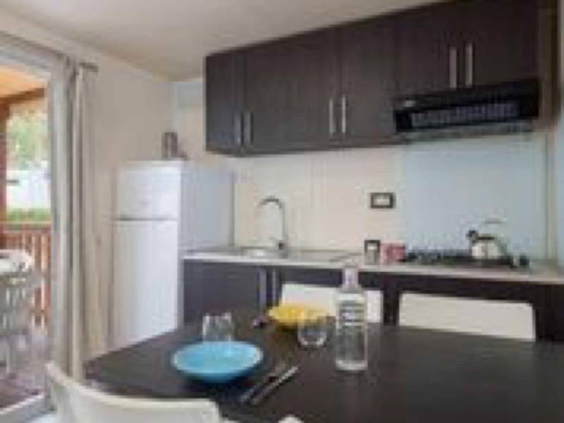 Kleine moderne Küchenkombination mit schwarzer Arbeitsplatte, weißen Stühlen und Balkon im Hintergrund.