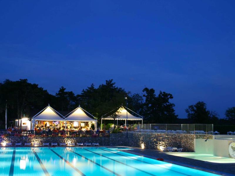 Beleuchtetes Freibad bei Nacht mit Pavillons und Bäumen im Hintergrund.