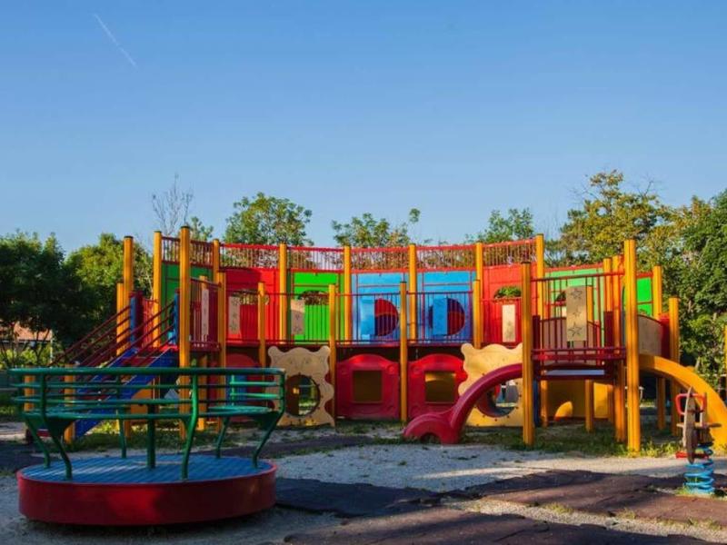 Bunter Spielplatz mit Klettergerüst, Rutschen und Karussell unter blauem Himmel.