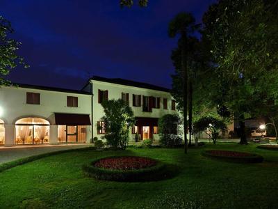 Budynek hotelu nocą z oświetlonym ogrodem i drzewami na trawniku.