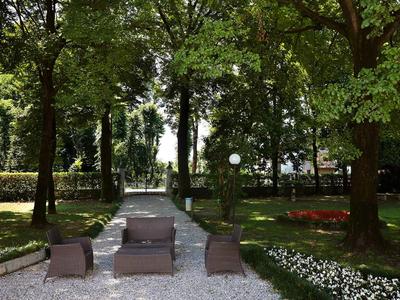 Garten mit bequemen Sesseln auf Kiesweg und dicht bewachsenen Bäumen im Hintergrund.