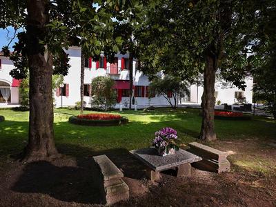 Miejsce do siedzenia z stołem i ławkami pod drzewami przed białym budynkiem hotelowym.