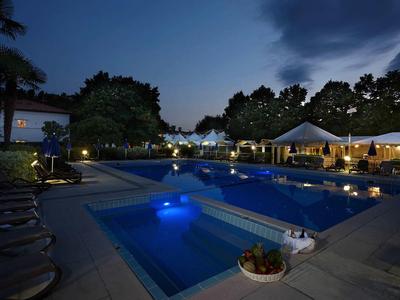 Beleuchteter Hotelpool mit Whirlpool nachts, umgeben von Pflanzen und Sitzbereichen.