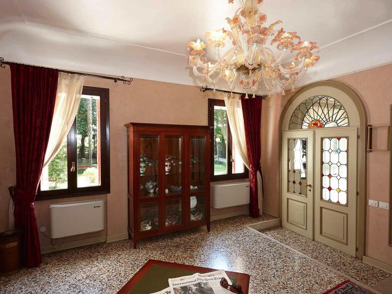 Elegancki hol hotelowy z żyrandolem, szafą wystawową i czerwonymi zasłonami.