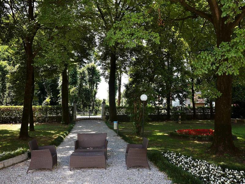 Wygodne meble ogrodowe na białej żwirowej ścieżce otoczonej zielonymi drzewami i kwietnikami.