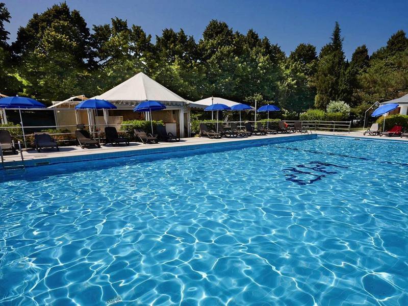 Duży basen z niebieską wodą i parasolami w ogrodzie.