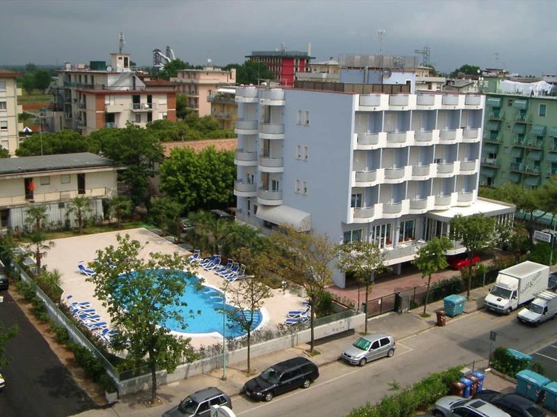 Mehrstöckiges Hotel mit Außenpool, umgeben von Bäumen und mehreren geparkten Fahrzeugen.