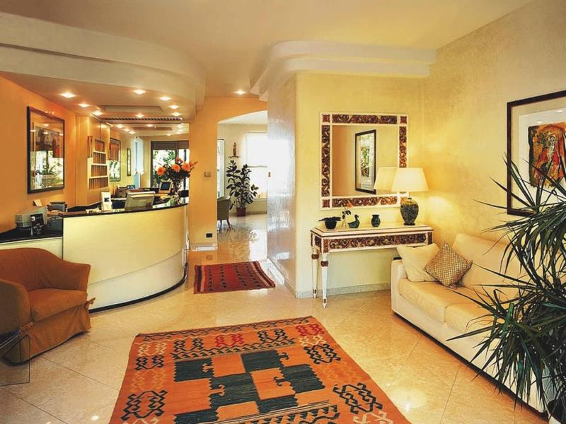 Helles Wohnzimmer mit beiger Couch, Teppich mit geometrischem Muster, Pflanze und Spiegel an der Wand.