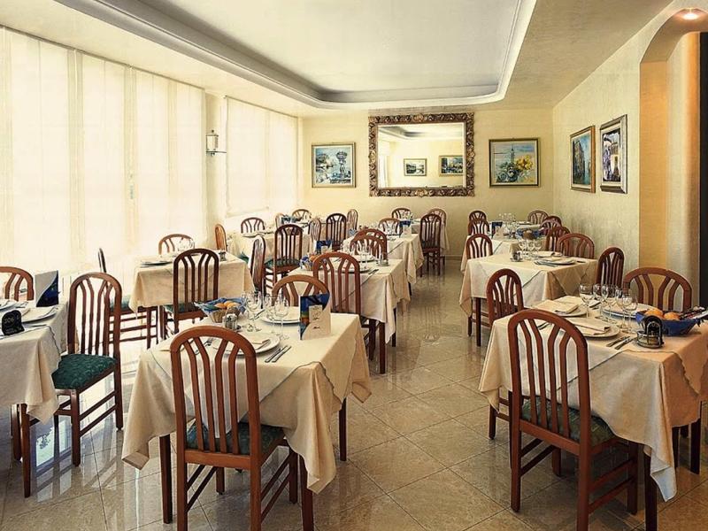 Ein leerer Speisesaal mit rechteckigen Tischen, beigen Tischdecken und Holzstühlen.