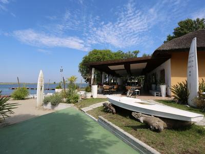 Hotelterrasse mit Tischen, Sonnenschirmen und Blick auf einen See bei klarem Himmel.