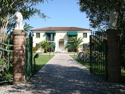 Eingangstor zu einem weißen Hotel mit Garten und Skulpturen auf steinernen Säulen