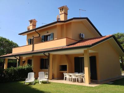 Zweistöckiges gelbes Ferienhaus mit Terrasse, Stühlen und Tisch unter blauem Himmel.