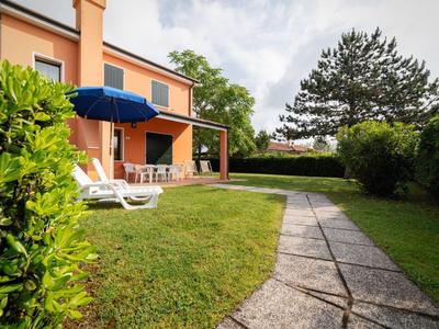 Gartenbereich mit Liegestühlen und Sonnenschirm neben einem zweistöckigen Haus bei bewölktem Himmel.