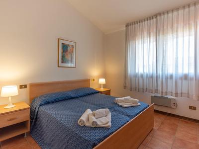 Hell eingerichtetes Hotelzimmer mit Doppelbett, zwei Nachttischen und Fenster mit weißen Vorhängen.