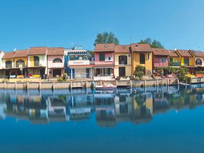 Bunte Häuser am Wasser mit perfekter Spiegelung und blauem Himmel bei einem Urlaubsort.