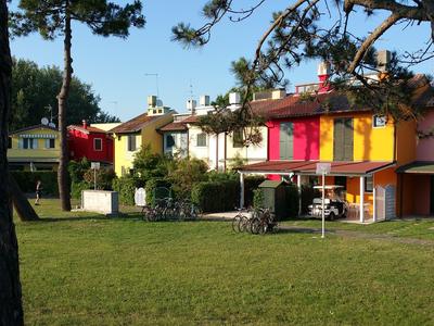 Mehrfarbiges Ferienhaus mit großen Fenstern und Grasfläche im Vordergrund unter Bäumen.
