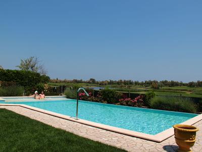 Schwimmbad mit klarem Wasser, umgeben von Rasen und blühenden Pflanzen unter klarem Himmel.