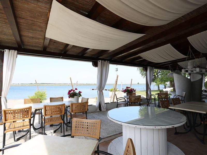 Überdachte Außenterrasse mit Tischen und Stühlen mit Blick auf das Meer und den Strand