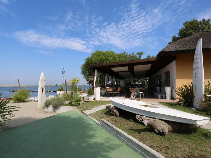 Außenbereich eines Hotels mit Terrasse, Sitzgelegenheiten und Blick auf einen See bei klarem Himmel.